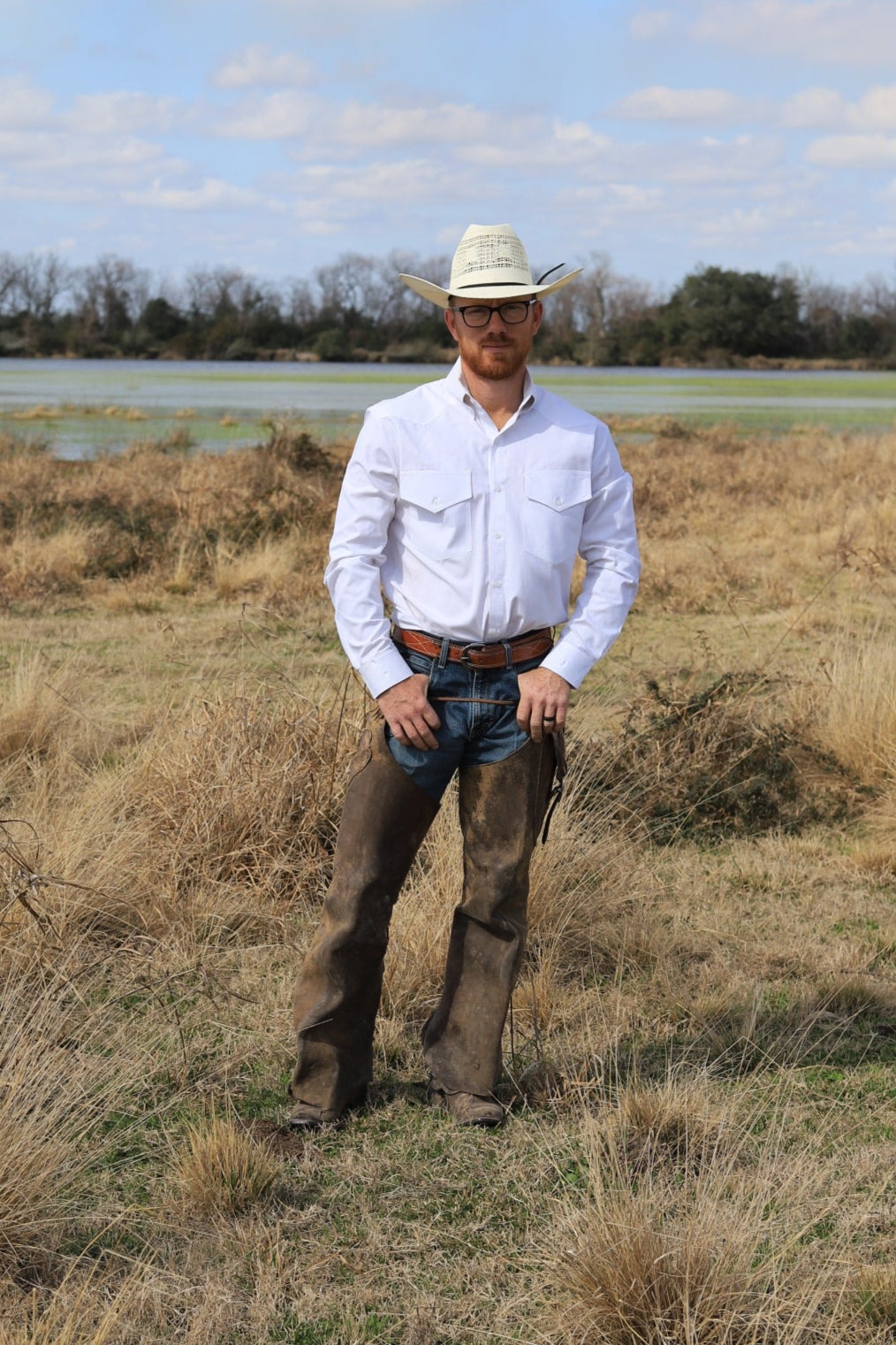 Man standing in a field with a horse, wearing a white shirt and hat.