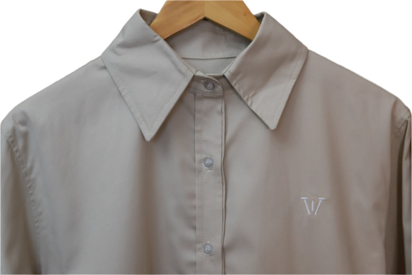 Beige shirt with a monogram on a wooden hanger against a beige background