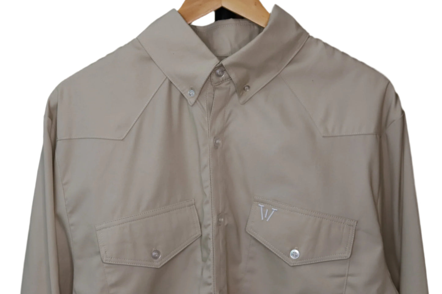 Beige shirt with two front pockets on a hanger against a brown background