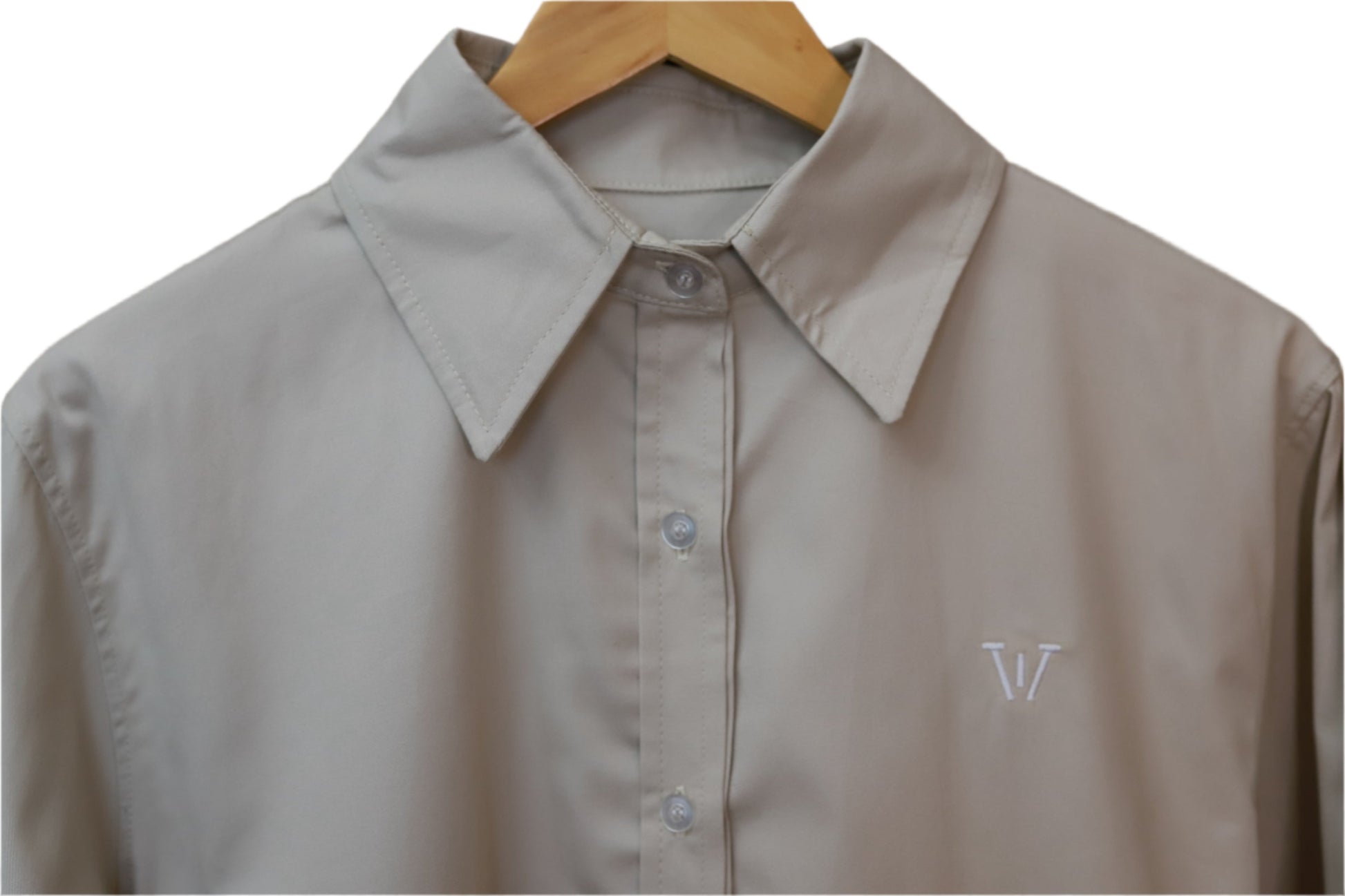 Beige shirt with a monogram on a wooden hanger against a beige background